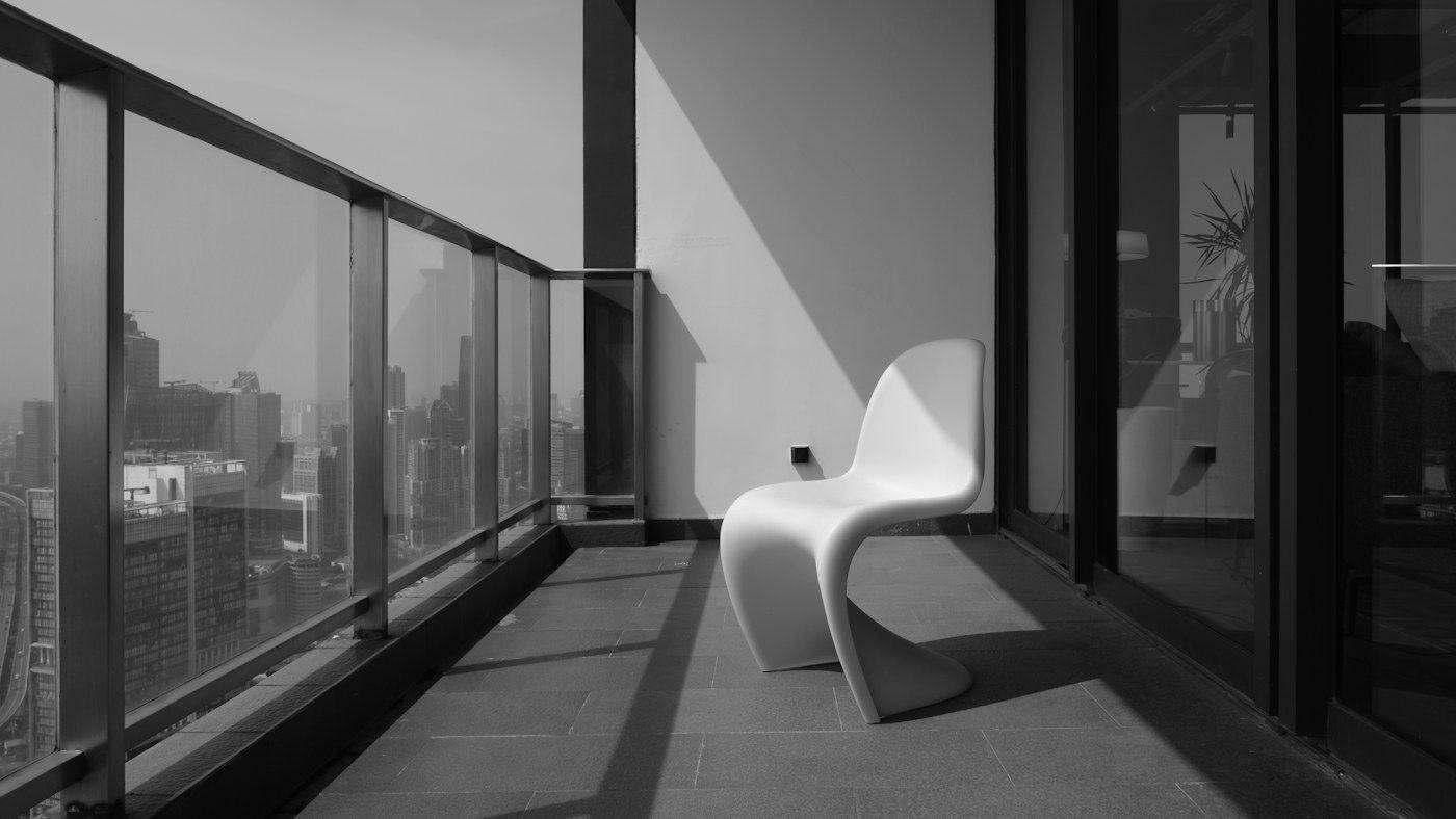 A single sculptural white chair on a narrow balcony overlooking the city, in black and white.