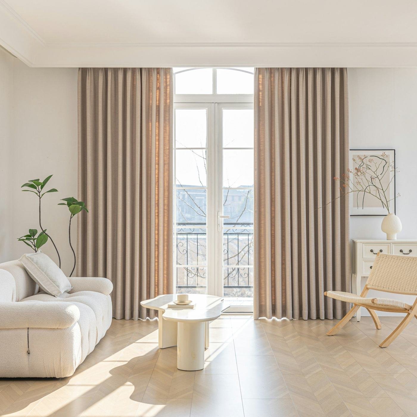 A cream sofa, small side table and wooden chair beside long linen curtains.