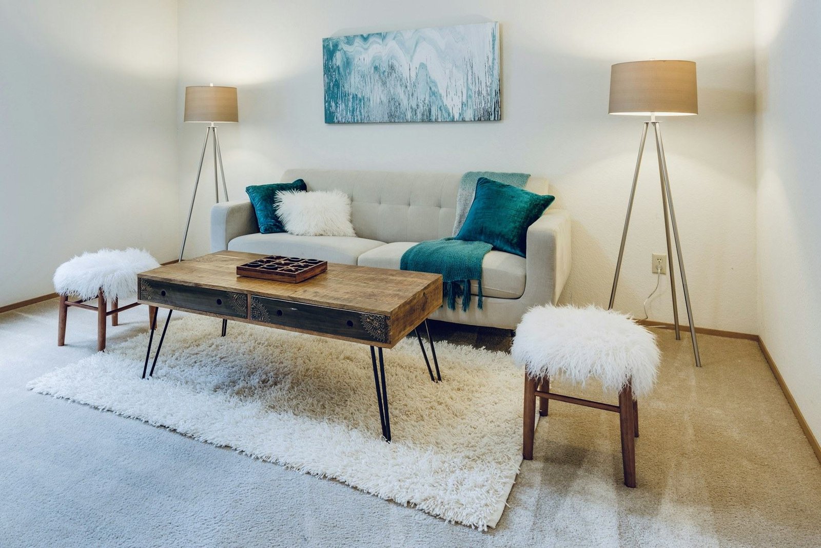 A cream sofa with teal cushions, a wooden coffee table and two floor lamps.