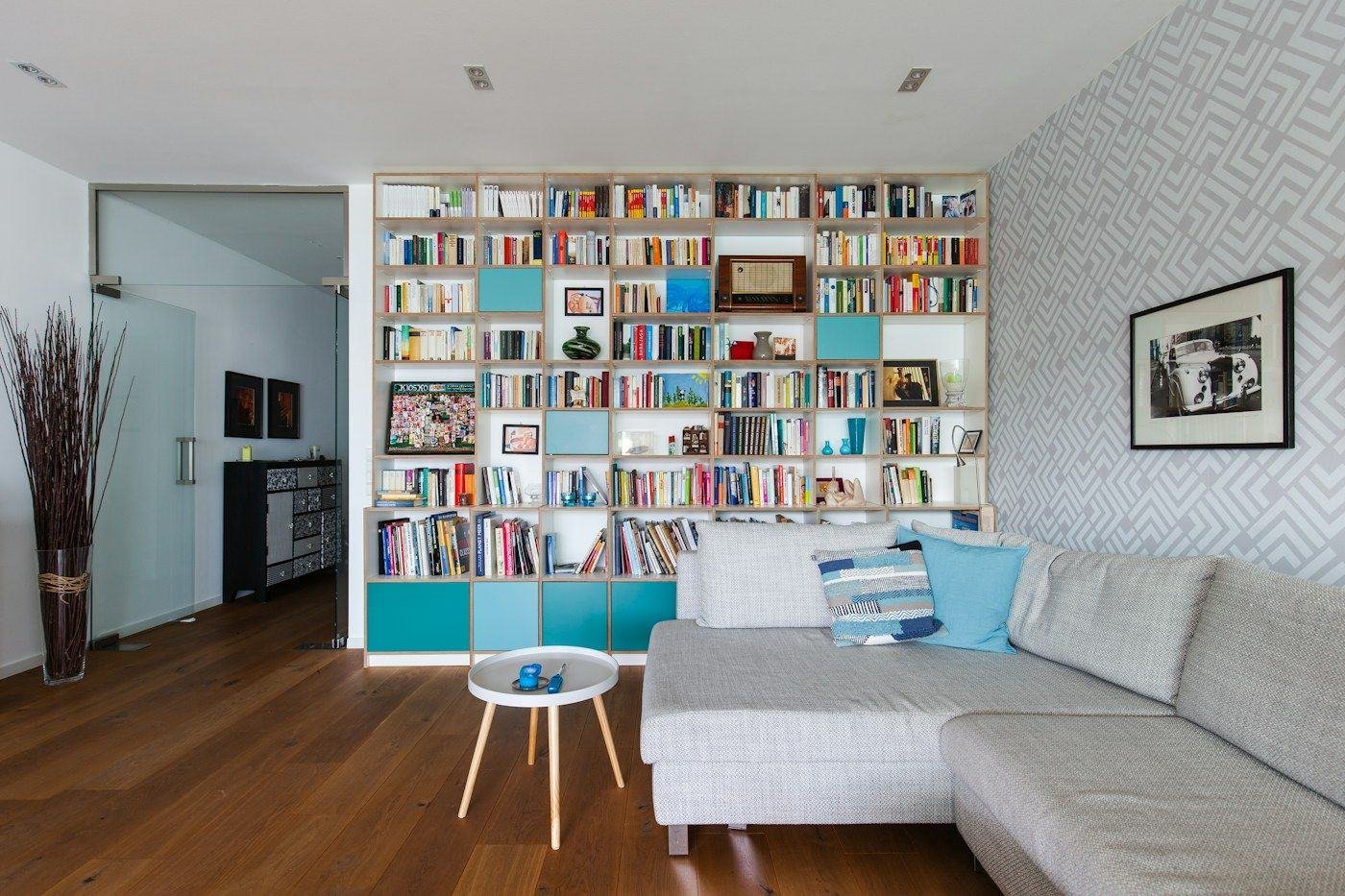 A wall of bookshelves with blue cabinet doors beside a gray sofa.