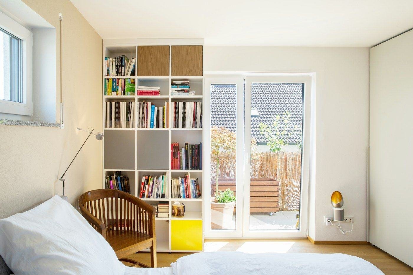 A tall white bookcase beside a glass door and a wooden chair in a bright room.